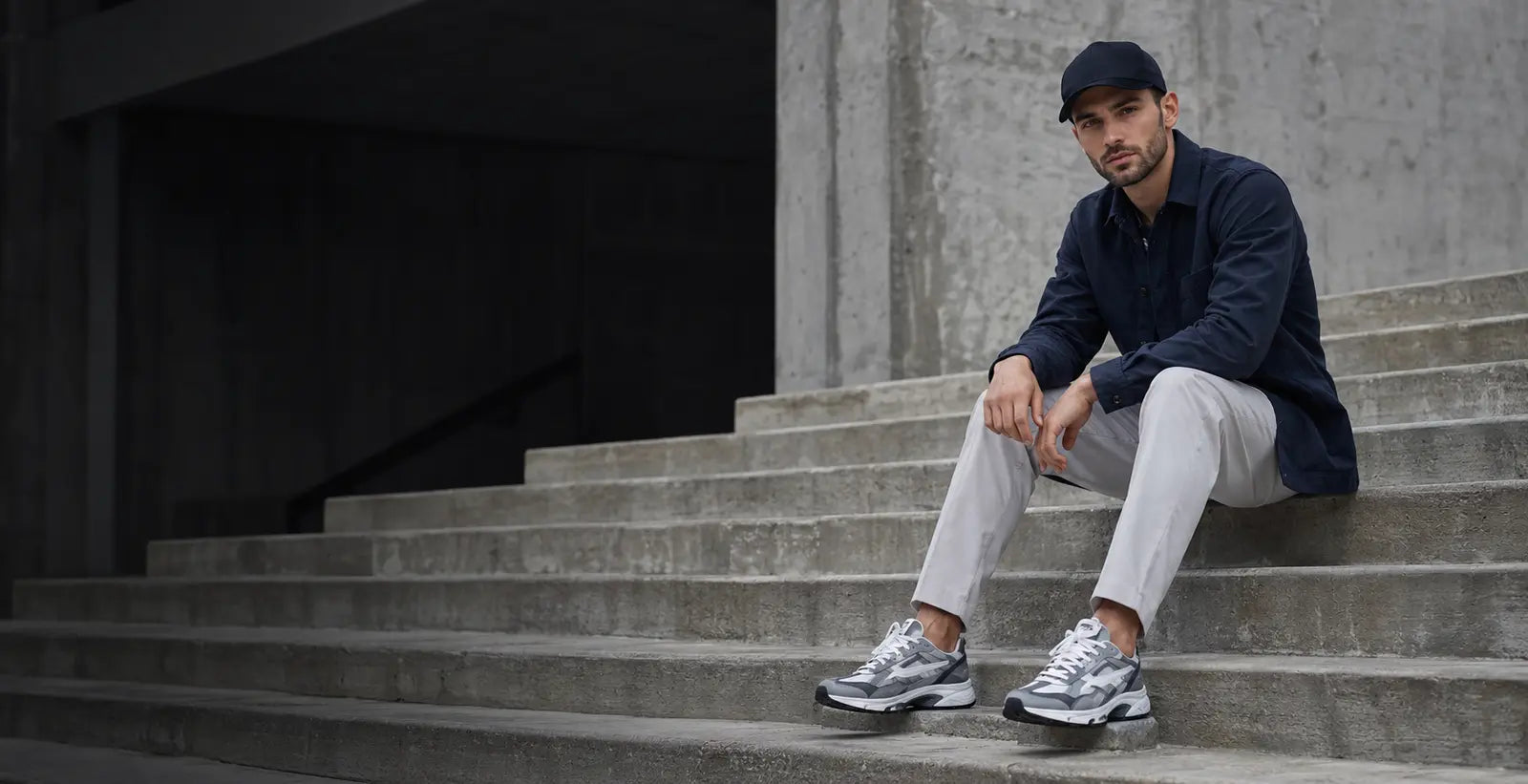 Man wearing grey trainers seated on concrete steps